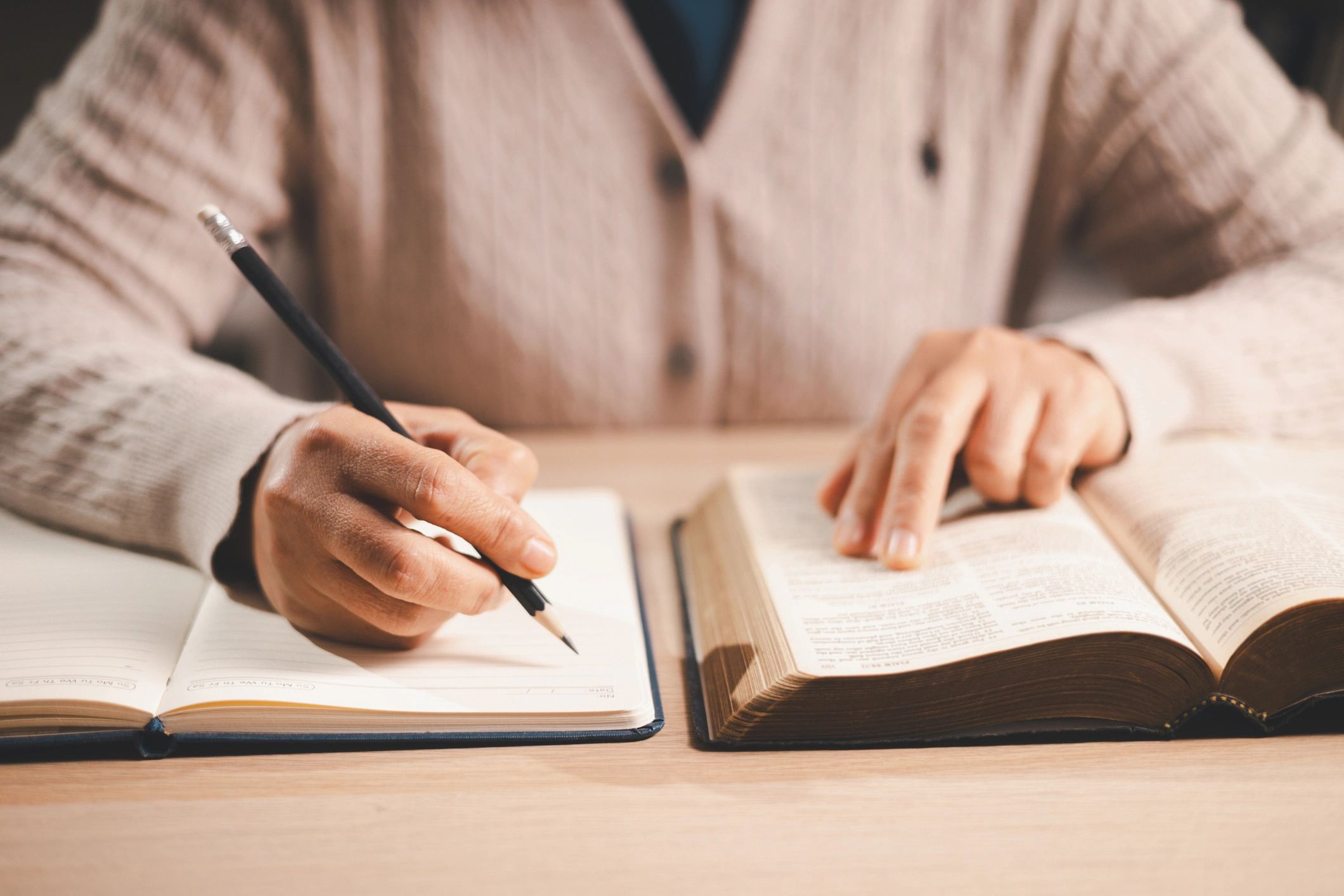 Manos tomando notas mientras estudia una Biblia abierta